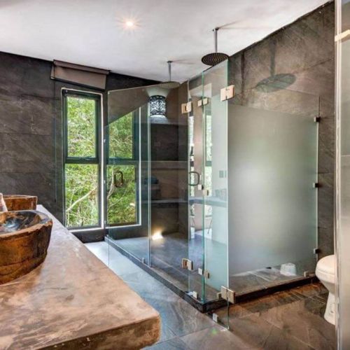 Bathroom with shower and toilet covered by glass doors and large windows facing the jungle